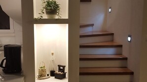 Un escalier avec des marches en bois et un mur blanc agrémenté d’étagères intégrées où sont disposées des plantes et des objets décoratifs.