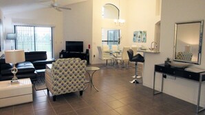 Un salon moderne comprenant un canapé, un fauteuil à motifs, un téléviseur et un coin repas avec une table et des chaises.