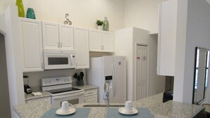 Une cuisine compacte avec des meubles blancs, un four à micro-ondes, un réfrigérateur et un petit îlot central agrémenté de deux chaises.