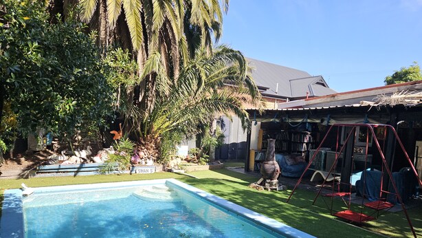 A swimming pool surrounded by a garden with palm trees and a swing set.