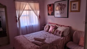 A bedroom with a large bed, a chair, and a window with sheer curtains.