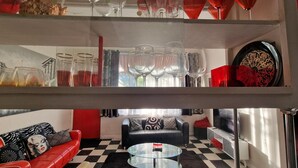 A modern living room with a checkered floor, a glass coffee table, a red sofa, and a black leather couch.