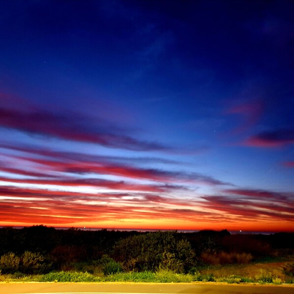 Un atardecer sobre un paisaje llano con un horizonte despejado y una carretera en primer plano.