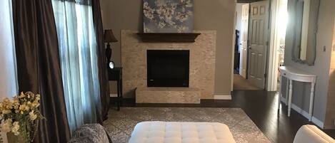 A hotel room with a fireplace, a bed, a sofa, a TV, and a hallway with a mirror.