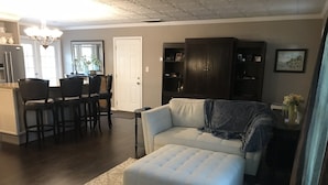 Ein Wohnzimmer mit einer Couch, einem Hocker und einem Essbereich mit Stühlen und einem Tisch.