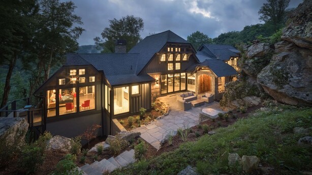 Une maison moderne dotée de nombreuses pièces, de grandes fenêtres et d’une façade en pierre.