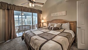 A bedroom with a large bed, a ceiling fan, a window with curtains, a bedside table with a lamp, and a door. - Lakefront Branson Getaway Near Marina & Fishing! (Branson)