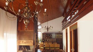 Un salon spacieux doté d’une cheminée, d’un plafond en bois et d’un coin repas avec des chaises et une table.