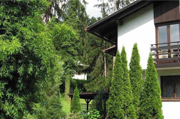A house with a white exterior, a balcony, and a garden with various trees.