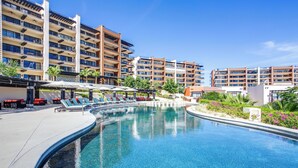 A swimming pool with lounge chairs and umbrellas, surrounded by multi-story buildings with balconies. - Quivira Golf Club Condo w/ Magnificent Ocean Views (Cabo San Lucas)