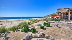 A beachside hotel with a patio area, a view of the ocean, and a thatched-roof building. - Quivira Golf Club Condo w/ Magnificent Ocean Views (Cabo San Lucas)