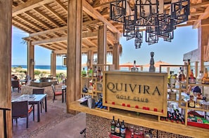 A beachside restaurant with a wooden structure, a sign reading "QUIVIRA GOLF CLUB", and a view of the ocean.