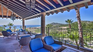 A covered outdoor seating area with wicker furniture and hanging lanterns, overlooking a coastal landscape. - Quivira Golf Club Condo w/ Magnificent Ocean Views (Cabo San Lucas)