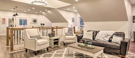 Un ampio loft con soffitto alto, una scala in legno, un'accogliente zona salotto con divano e poltrone, e un lampadario.