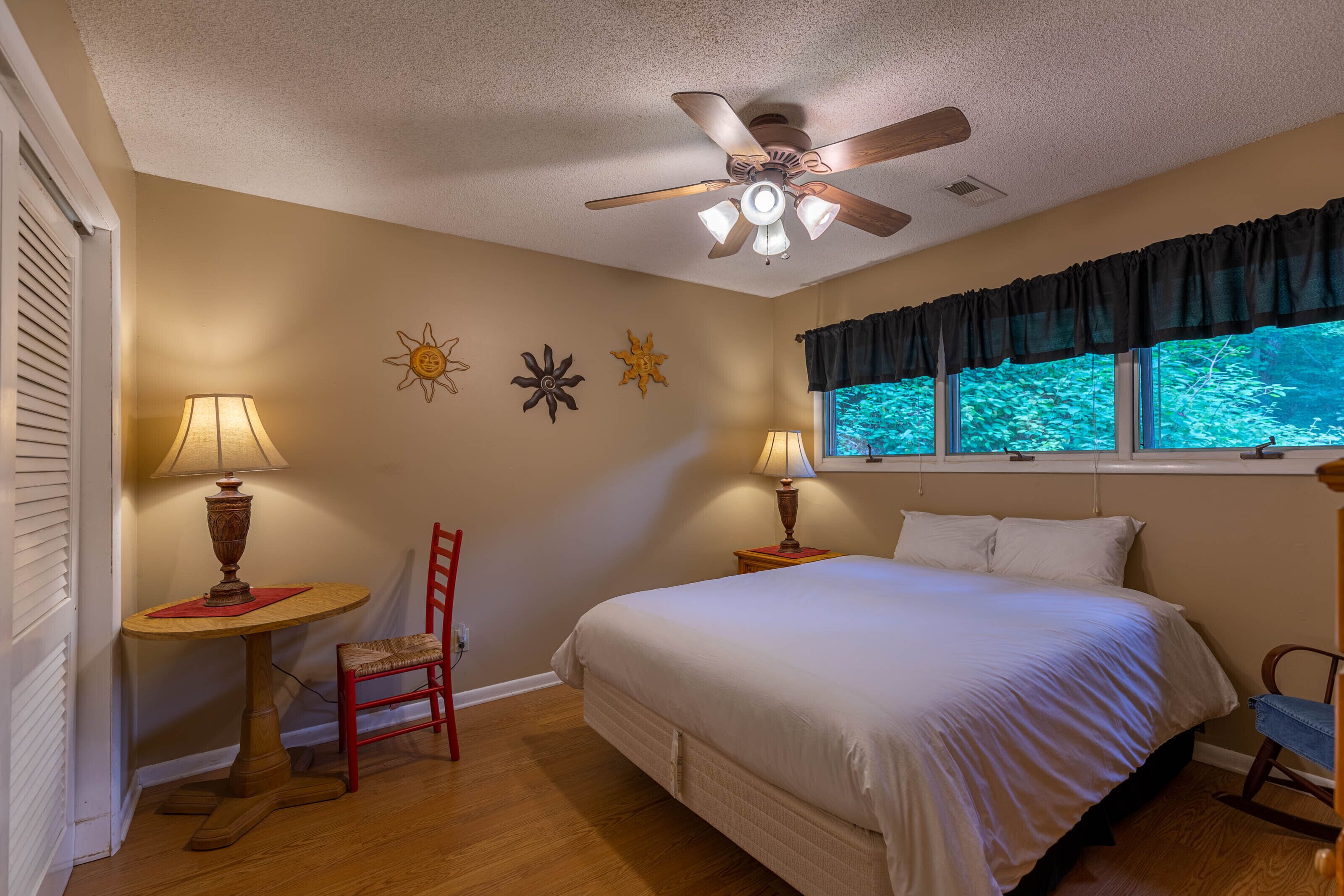 A bedroom with a bed, two bedside lamps, a ceiling fan, a window with curtains, and a wall with decorative sun motifs.