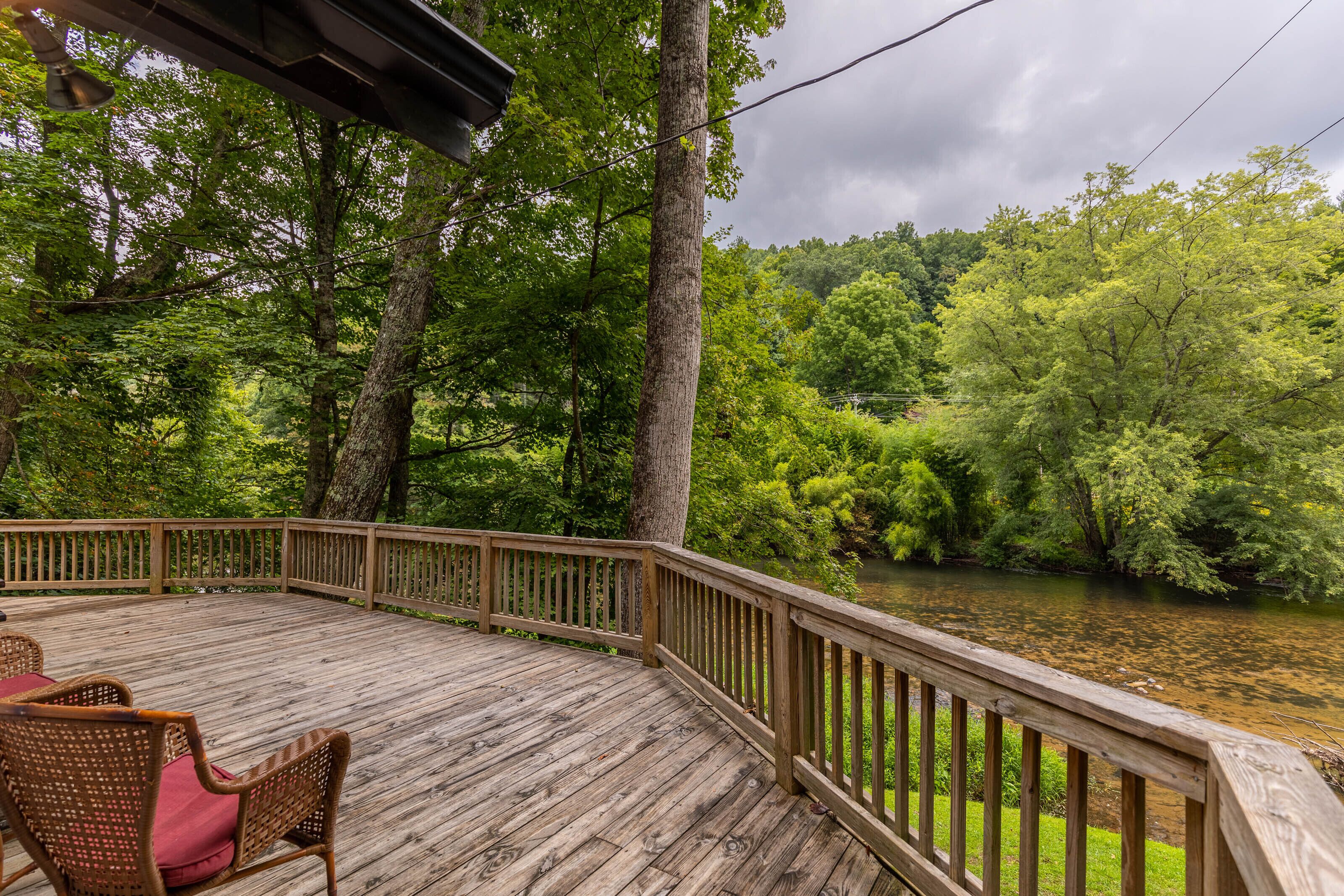 A wooden deck with wicker chairs, overlooking a river surrounded by dense forest.