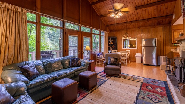 A cozy cabin interior with a leather sofa, ottomans, a dining area, and a kitchen. - Rivers Edge in Todd - Home with hot tub- Enjoy the River from your front porch rocker (Todd)