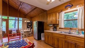 A wooden cabin kitchen with a dining area, a refrigerator, and a window with curtains. - Rivers Edge in Todd - Home with hot tub- Enjoy the River from your front porch rocker (Todd)