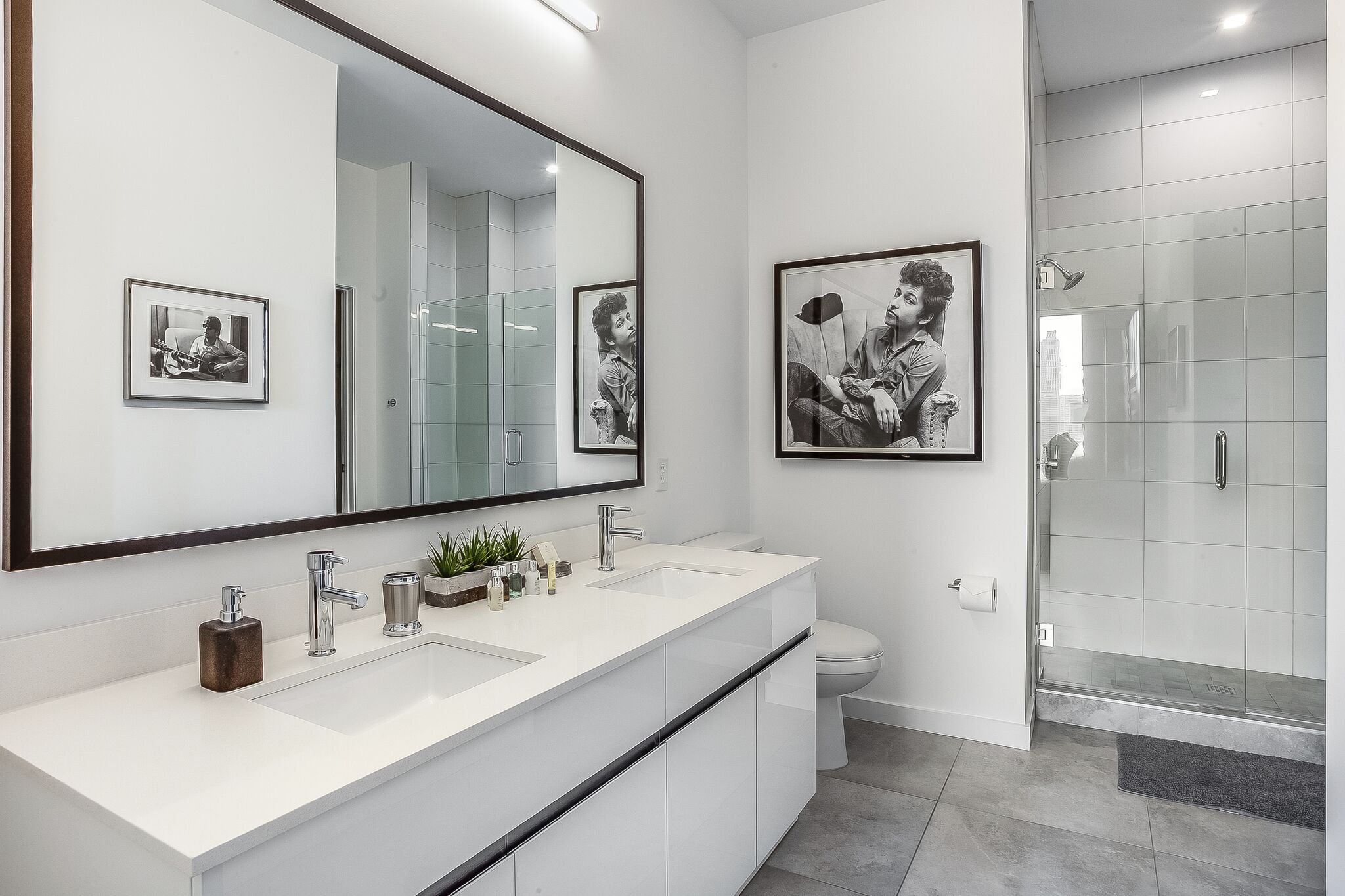 Ein modernes Badezimmer mit einem großen Spiegel, zwei Waschbecken, einer Toilette und einer Duschkabine.