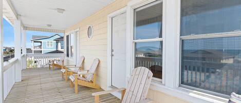 A wooden deck with four Adirondack chairs, a white door, and a large window.