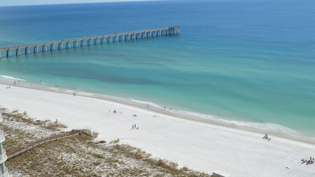 A beach with a pier extending into the ocean, sandy beach, and a few people.
