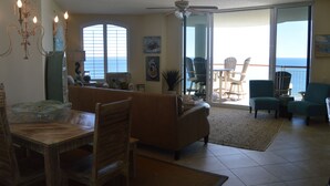 A spacious living area with a dining table, chairs, a sofa, and a balcony with chairs.