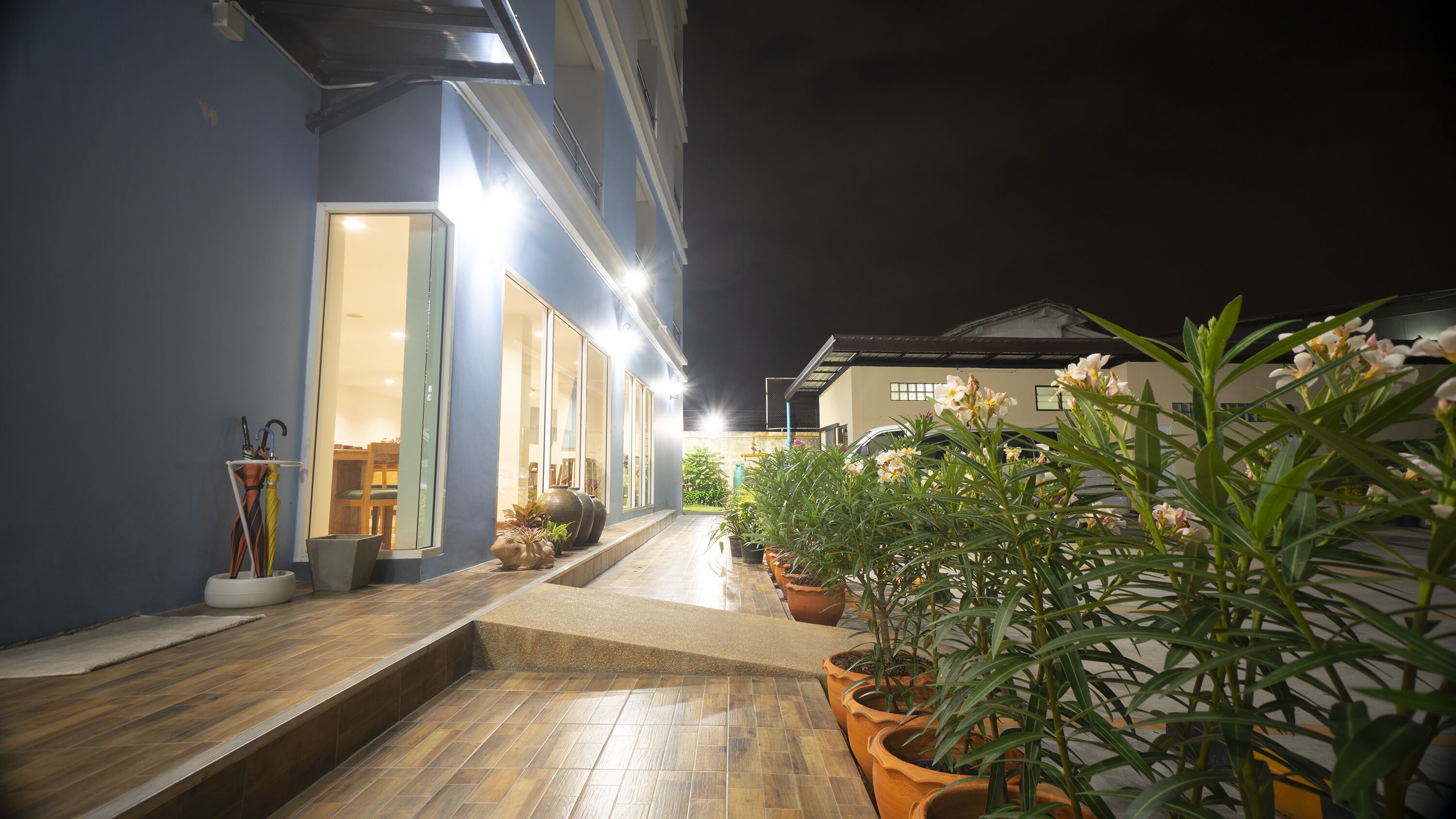 A well-lit outdoor area with potted plants and umbrellas, leading to a building entrance.