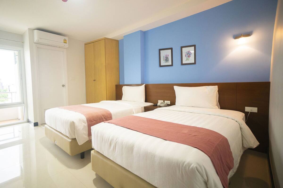 Habitación de hotel con dos camas, un armario, un teléfono y una ventana con vistas.