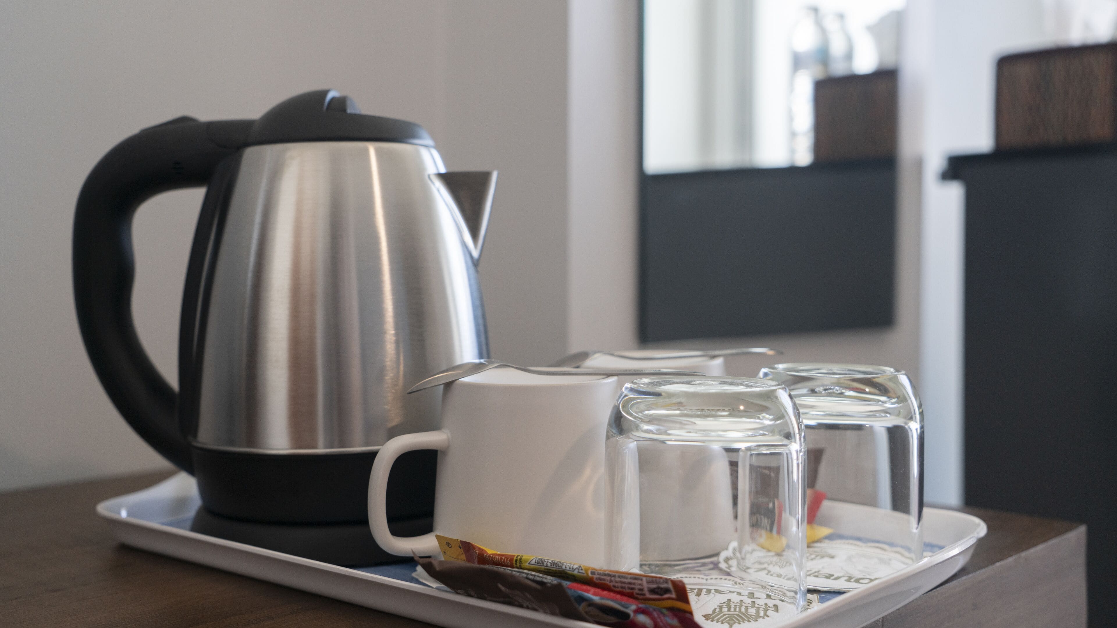 Une bouilloire en acier inoxydable, deux tasses blanches et deux verres transparents, le tout disposé sur un plateau.