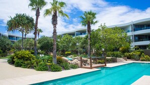 Una piscina rodeada de palmeras y abundante vegetación, con edificios modernos al fondo.