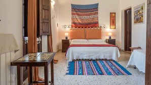 A bedroom with a bed, two bedside tables with lamps, a patterned tapestry, a wooden headboard, and a tiled floor. - Beautiful private villa for 14 people with WIFI, private pool, TV, terrace and pets allowed (Buseto Palizzolo)