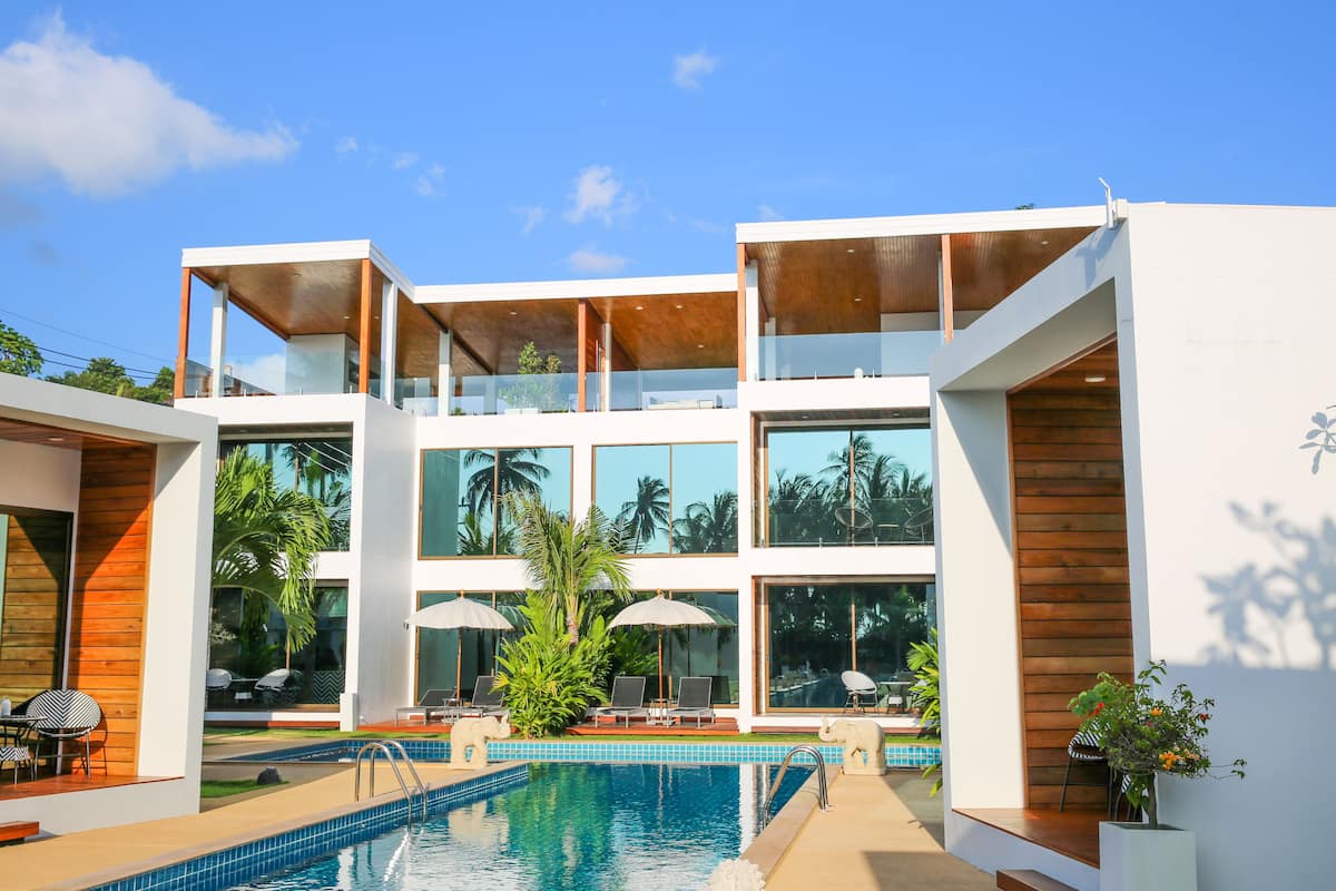 Un edificio moderno de varios pisos con piscina, mobiliario exterior y ventanas amplias.