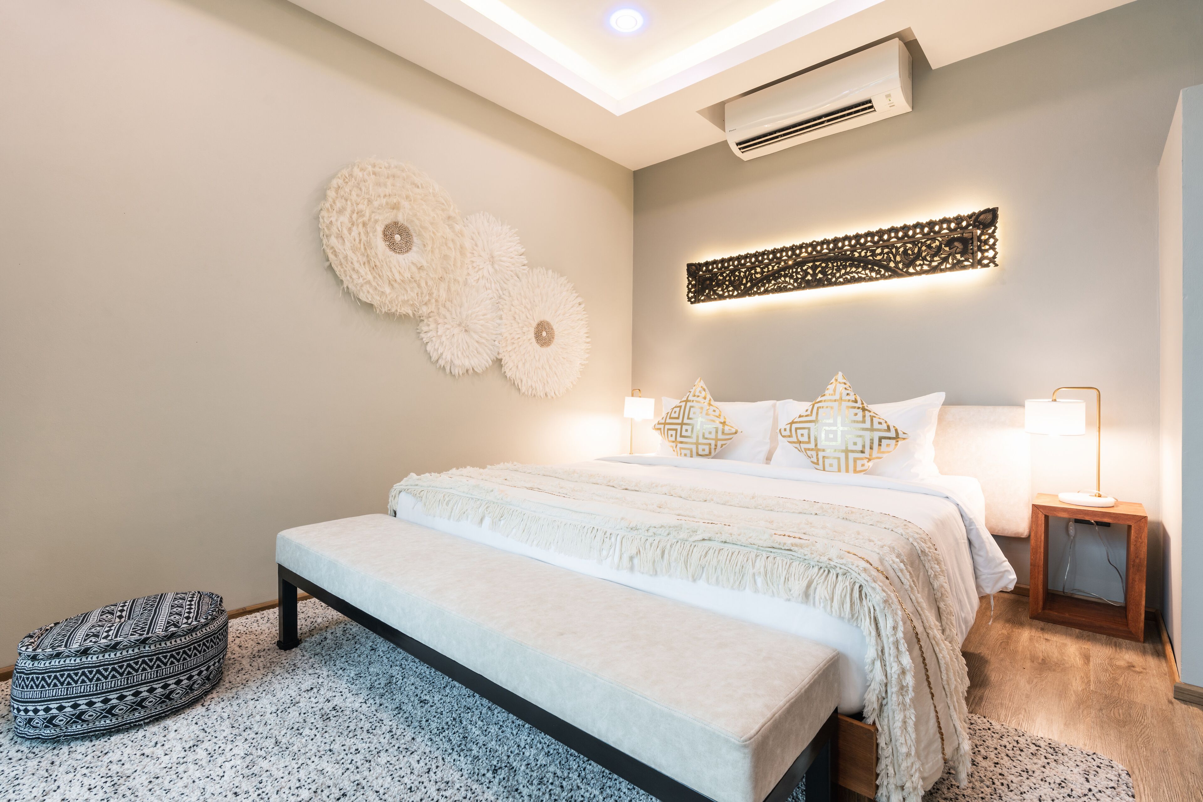 Une chambre moderne avec un grand lit, un banc et un climatiseur fixé au mur.