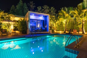 Ein Pool mit einer modernen Hausstruktur in der Nähe, umgeben von Palmen und Sitzgelegenheiten im Freien.
