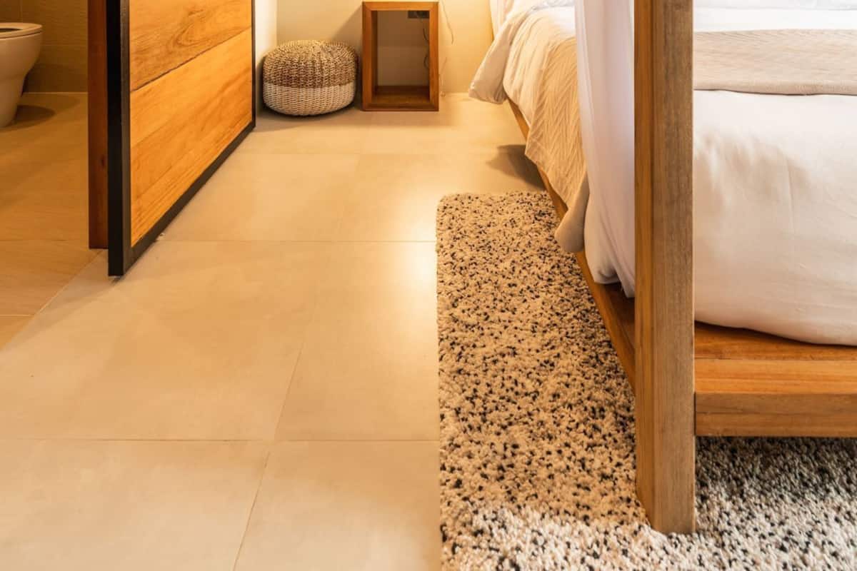 Un dormitorio con un armario de madera, una mesita de noche con lámpara, una cama con ropa de cama blanca y una pequeña alfombra.