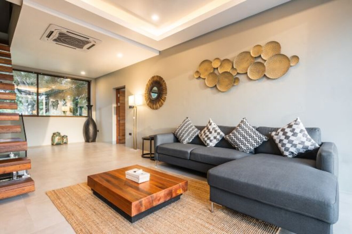 A modern living room with a grey sectional sofa, patterned cushions, a wooden coffee table, and a wall art piece.