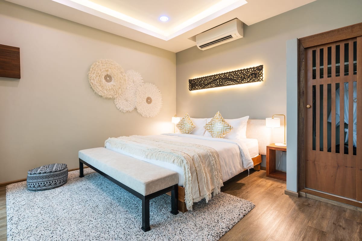 Un dormitorio moderno con cama, mesitas de noche, un banco y decoración en la pared.