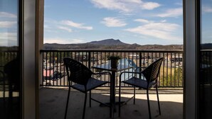 Varanda com duas cadeiras e uma pequena mesa, com vista para um estacionamento e montanhas ao longe.
