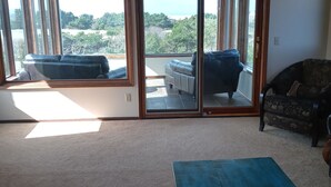 A spacious living area with a ceiling fan, a blue table, and a view of the outdoors through large sliding glass doors. - One block to the beach, beautiful 3bd/3ba house with view, come relax and enjoy (Warrenton)