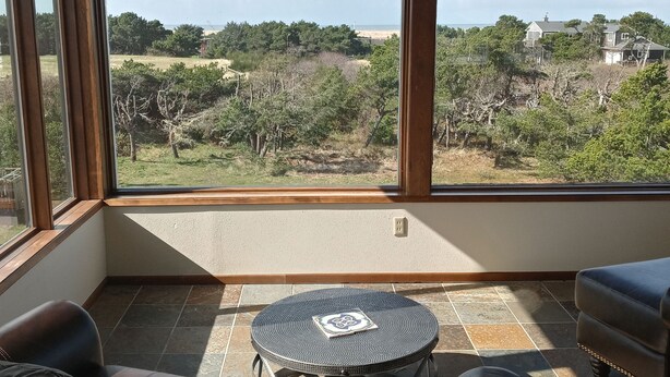 A room with a large window, a small round table, a sofa, and a ceiling fan. - One block to the beach, beautiful 3bd/3ba house with view, come relax and enjoy (Warrenton)