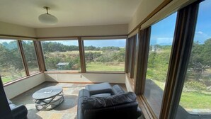 A sunroom with a view of a grassy landscape, a black leather sofa, and a small round table. - One block to the beach, beautiful 3bd/3ba house with view, come relax and enjoy (Warrenton)