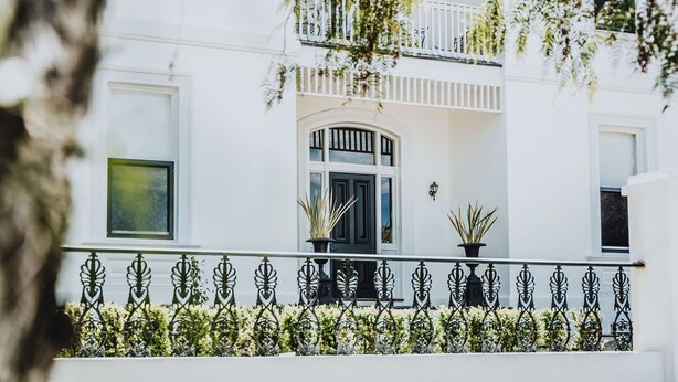 Un edificio blanco con balcón, plantas en macetas y barandilla de hierro forjado.