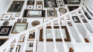 Una escalera con balaustres blancos y una pared decorada con numerosas fotografías enmarcadas.