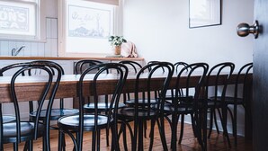 Un comedor con una mesa de madera y sillas de metal negro, una ventana con vistas, y un cuadro en la pared.