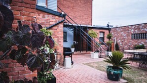 Un edificio de ladrillo con patio, mobiliario exterior y una escalera que conduce a un nivel superior.