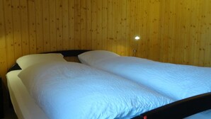 A room with two single beds, wooden walls, and a small bedside table with a lamp. - Apartment Reseda by Interhome (Lenk)