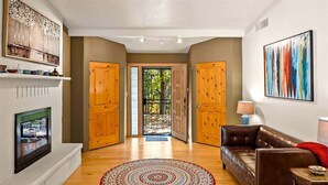A hallway with a patterned rug, a brown leather sofa, and wooden doors leading to an outdoor area. - Rooftop Deck, Sedona Views, Fenced Yard +Pets! (Sedona)
