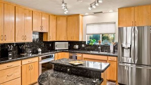 A kitchen with wooden cabinets, a granite countertop, a stainless steel refrigerator, and a window with blinds. - Rooftop Deck, Sedona Views, Fenced Yard +Pets! (Sedona)