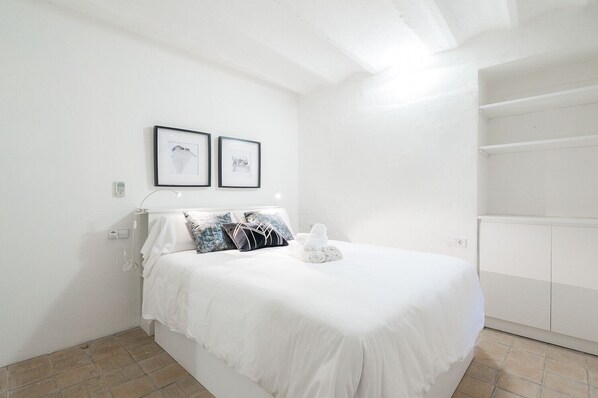 Une chambre à coucher blanche avec un lit, deux tableaux encadrés au mur et une armoire blanche.