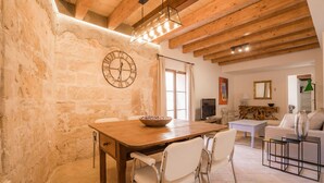 A rustic dining area with a wooden table, white chairs, and a stone wall. - VINTAGE PALMA PALACE (SUPERIOR 4) by Priority (Palma de Mallorca)